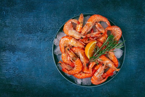 Freshly frozen shrimp on ice, with lemon and rosemary, on a dark blue table, top view, no people
