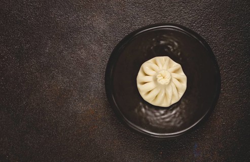 One khinkali, on a black plate, top view, cooking concept, Georgian cuisine