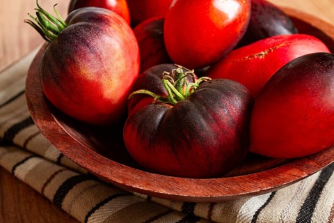 Freshly picked tomatoes, of the Black Beauty variety, in a wooden bowl, close-up, on the kitchen