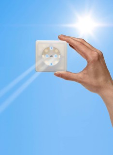 Symbolic solar energy theme showing the sun and sky with human hand holding a electrical socket
