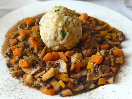 Vegetable stew with mushrooms and bread dumplings on a white plate, seasoned and served Lower