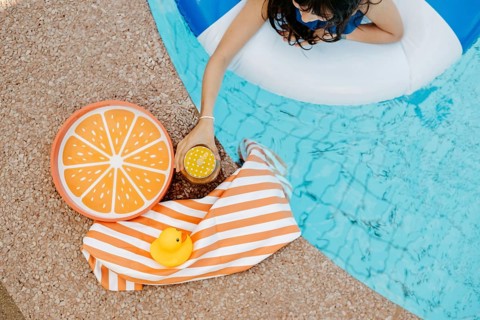 Girl with a swimming tyre in the pool, a striped bath towel, a swimming duck, a cocktail and an