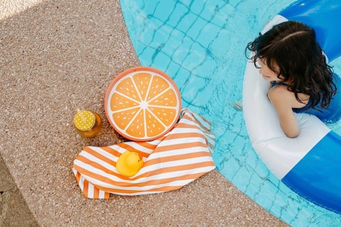 Girl with a swimming tyre in the pool, a striped bath towel, a swimming duck, a cocktail and an