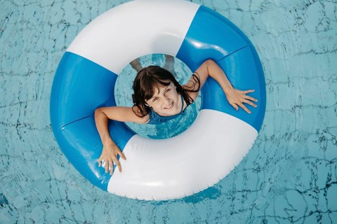 Girl, 10, in the pool, looks out of a blue and white striped swimming tyre