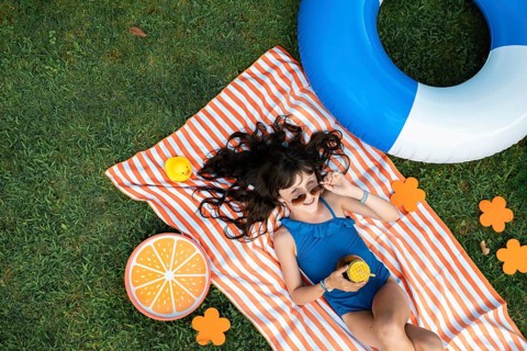Girl, 10, with sunglasses in a blue swimming costume, lying relaxed in the meadow with a cocktail