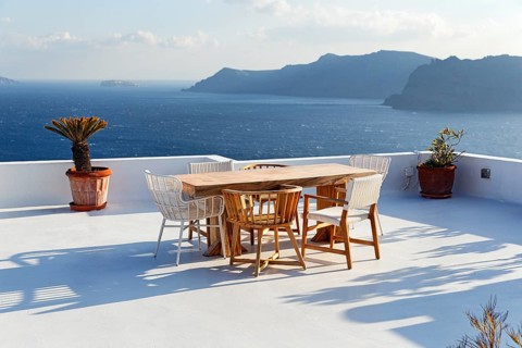 Wooden table and various chairs on a white terrace by the sea, view of the caldera, Oia, Santorini,