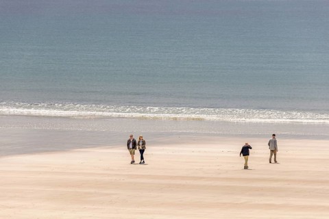 Group of people walking in the sunshine on a sandy beach with rolling waves at the sea, Crozon