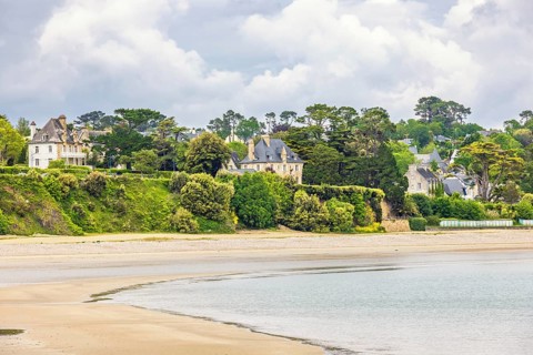 House by a sandy beach by the sea with lush green trees at the coast, Morgat, Crozon peninsula,
