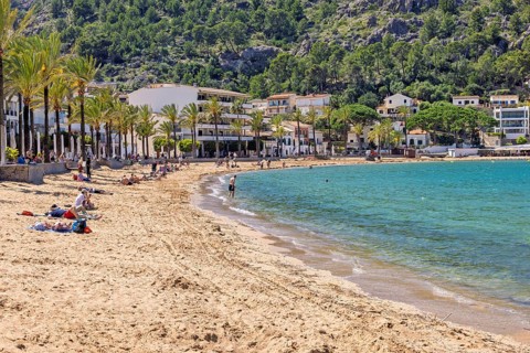 Sand beach with tourists at a tourist resort with houses at the shore line and palm trees a sunny