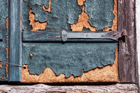 Weathered detail of an old shutter with rusty hinge and peeling paint, Alsace, France