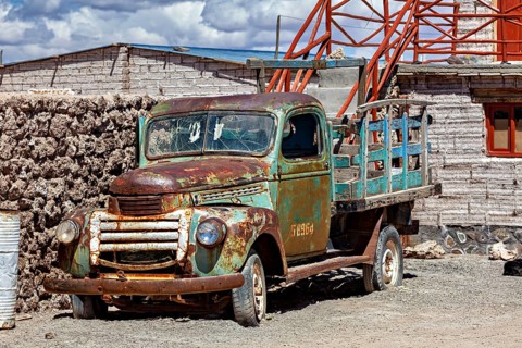 Rusty historic lorry next to an old brick building with outside stairs under a blue sky, Old lorry