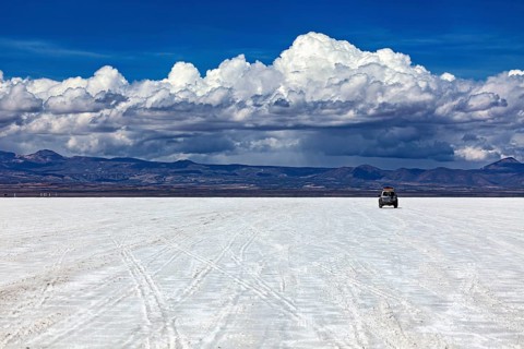 An off-road vehicle drives across an endless salt flat under a sky full of clouds, The endless