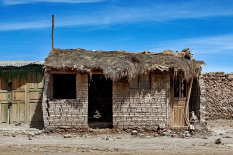 Abandoned hut with a thatched roof and mud bricks under a clear blue sky, a village on the