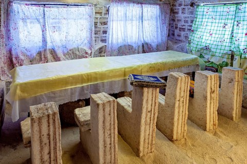 Long stone table with matching stone chair set in a bright, rustic room with patterned curtains,