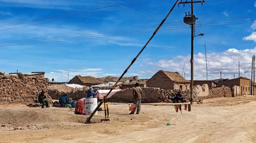 Small desert town with clay-like houses under a blue sky, power lines and local people, A village