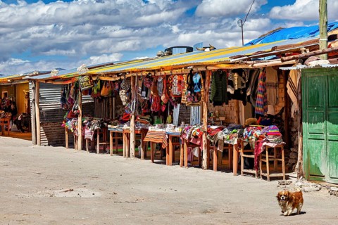 Colourful market stalls along a road under a cloudy sky, lively rural scene, market stall for