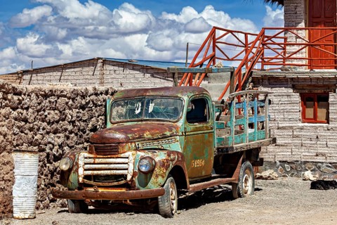 Rusty old lorry in front of a rustic building in a desert environment with blue sky and clouds, Old