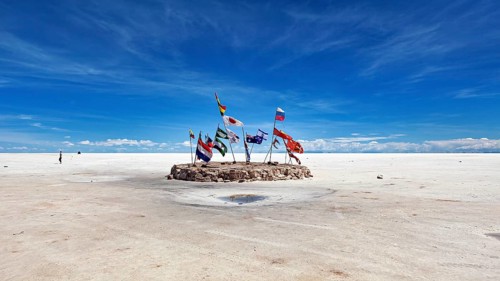 Flags in a vast salt lake under a clear blue sky with scattered clouds, international flags in the