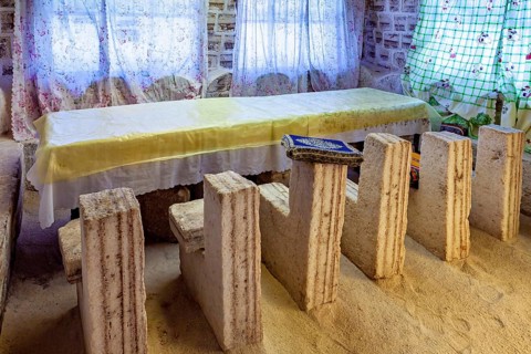 Long stone table with matching stone chair set in a bright, rustic room with patterned curtains,