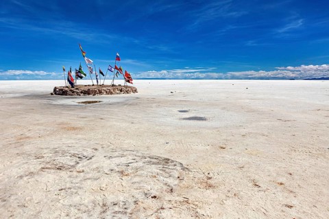Flags in a vast salt lake under a clear blue sky with scattered clouds, international flags in the