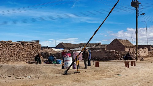People in a desert town with clay-like buildings and a street lamp under a blue sky, A village on