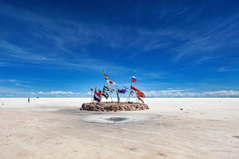 Flags in a vast salt lake under a clear blue sky with scattered clouds, international flags in the