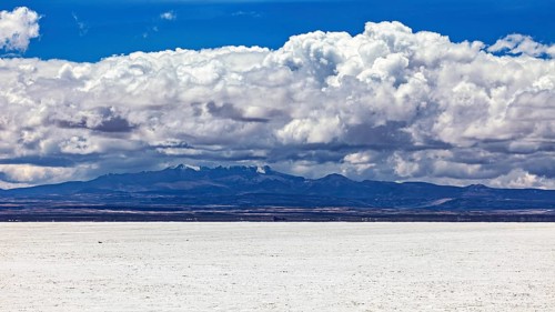 Majestic cloud formation over a flat, white salt landscape with a mountain backdrop, The endless