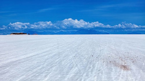 Vast salt flat with a mountain range on the horizon and clouds under a clear sky, The endless