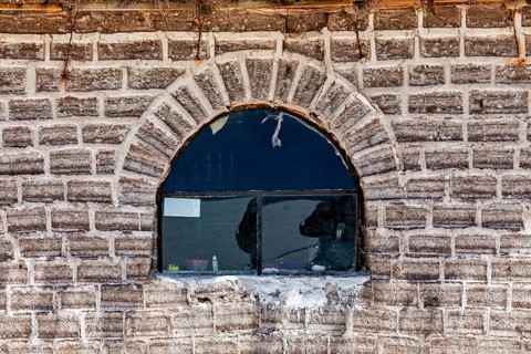 The rustic window with reflection is located in a curved brick wall, A wall made of salt bricks in