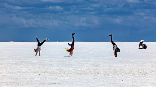 People doing handstands on a vast salt flat under a dramatic sky, The endless expanses of the salt