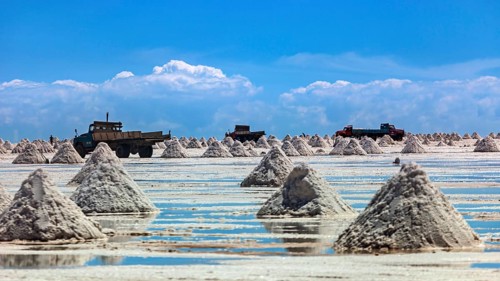Lorries and salt hills on a reflective salt flat under a blue sky and clouds, The endless expanses