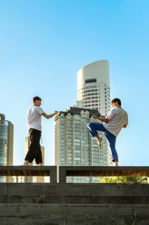 Vertical shot of two young men performing martial arts forms in a city setting