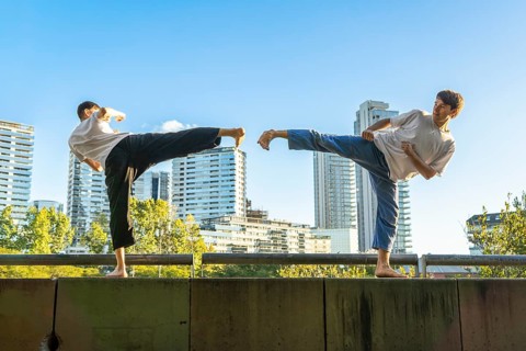 Young men executing synchronized Taekwondo kicks with urban buildings in the background