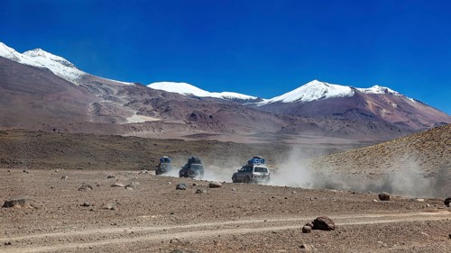 Off-road vehicle driving through a remote desert landscape with snow-capped mountains in the