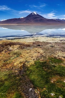 Volcano in front of a clear lake whose surface reflects the summit and the blue sky, The Laguna