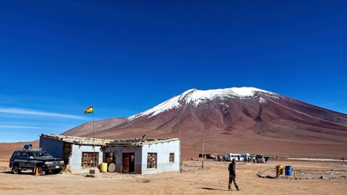 A remote mountain region with a simple building and a vehicle, overlooked by a clear blue sky, The