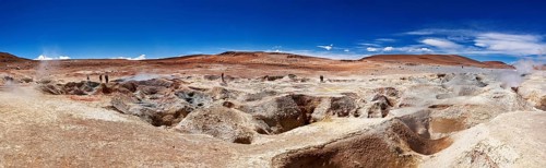 Panoramic view of a geyser field in a barren desert landscape under a bright blue sky, The mud