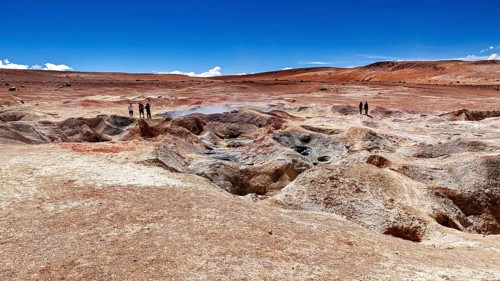 Landscape with geysers in a desert, two people on the horizon, clear blue sky, The mud volcanoes