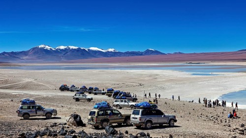 Several off-road vehicles parked in a desert landscape with mountains and snow-capped peaks under a