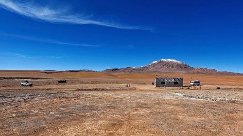 Vast, lonely desert landscape with a small building and snow-capped mountains in the background,