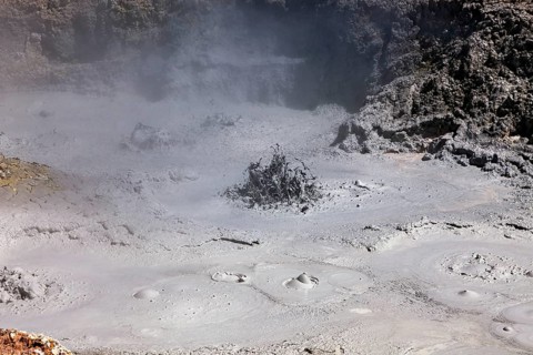 Steam rises from a geyser in the grey, cracked surface of the earth, The mud volcanoes and