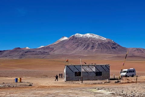 A small migration building in a vast desert landscape with snow-capped mountains, The border