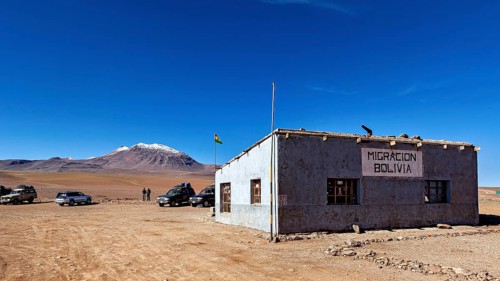 A small border building in a barren landscape with snow-capped mountains in the background, The