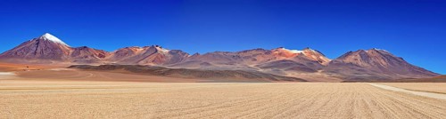 Sweeping panoramic views of a series of mountains, including snow-capped peaks, under a clear sky,