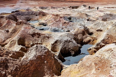 Hot springs with mineral colours in a desert, group of people in the background, The mud volcanoes
