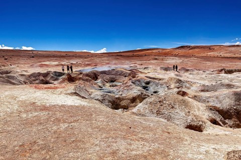 A glistening sky over vast desert plains with geysers and people in the distance, The mud volcanoes