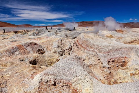 Steam rises from craters in a vast geothermal desert landscape, the mud volcanoes and fumaroles on