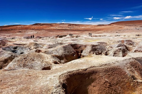 Vast, barren rocky landscape in the desert, two people on the horizon, blue sky, the mud volcanoes