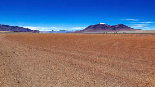 A wide, dry expanse of sand with a mountain on the horizon under a clear blue sky, The landscape of