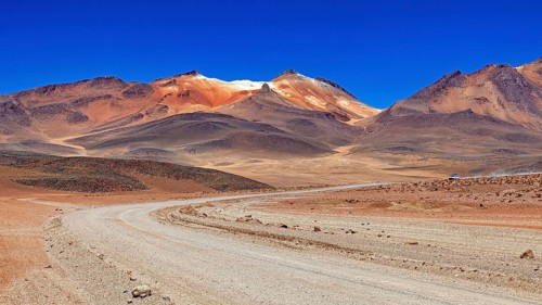 A sandy road winds its way through a vast, barren landscape under a bright blue sky, The landscape